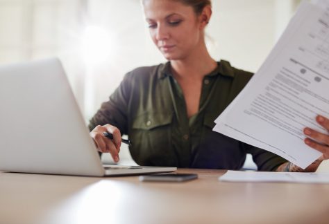 Young woman with documents working on laptop